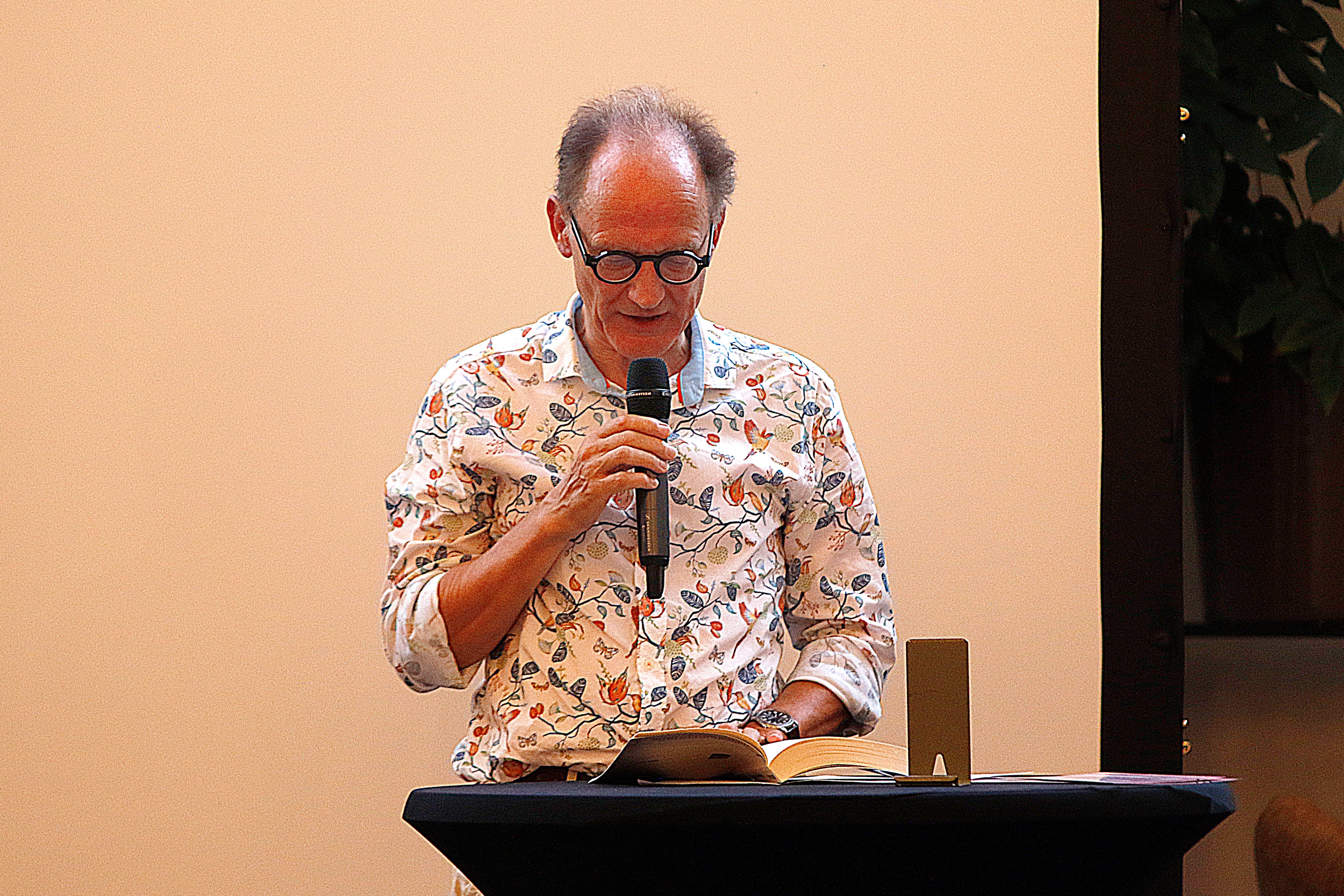 Cees Baas leest voor uit Code Berna achter een lessenaar met microfoon